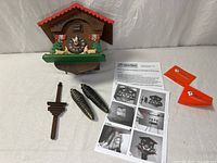 Front view of chalet cuckoo clock with weights, pendulum, manual and cards
