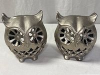 Front view of both silver-tone owl figurines showing cutout eyes and feather pattern