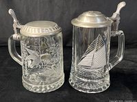 Front view of both etched glass steins showing motifs and pewter lids