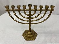 Front view of brass menorah showing 9 candle holders and hexagonal base