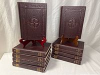 Two stacks of matching leather-bound encyclopedia volumes with decorative covers and one book on stand each side