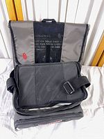 Timbuk2 folder bag open showing interior and shoulder strap with Craftsman bag below
