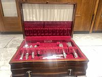 Open wooden chest showing flatware in red velvet slots