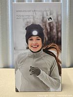 Retail box front showing woman wearing dark grey beanie with illuminated LED