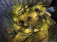 Top-lit view showing illuminated frosted wreath, pine cones, twigs, and battery pack