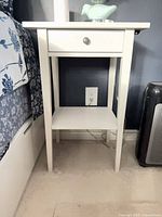 Nightstand beside bed, showing drawer front and shelf