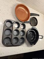 All items laid on countertop: two muffin tins, two fry pans, chicken roaster with cone and tongs visible