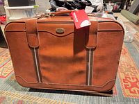 Front view of brown suitcase with handle, stripes and tag