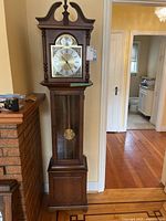 Full view of Howard Miller grandfather clock showing case, dial, pendulum and weights