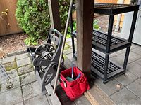 Hose reel frame, long-handle tool, red tool tote with hand tools next to black resin shelf