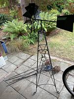 Overall view of black metal windmill tower with rotor and tail on patio, stake ornaments laid beside