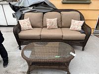 Three-seat wicker sofa with cushions and pillows beside matching oval glass-top coffee table