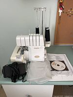 Serger with foot pedal, threads, manuals, CD, accessory pouch on tabletop
