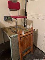Red vinyl chair atop grey laminate table with wooden folding chair leaning
