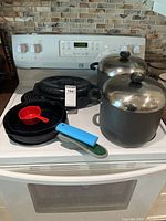 All cookware items grouped on stove: two cast iron pans, two stock pots with lids, small speckled roasting pan