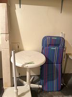 Round white plastic patio table beside folded striped cushions and umbrella pole