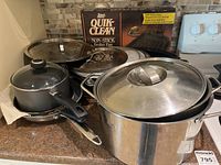 Overall view of cookware stack including stock pot, saucepan, frying pans, lids, splatter screens and boxed broiler pan