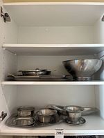 Cabinet view showing all stainless steel serving pieces on two shelves