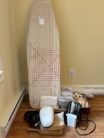 Ironing board with items at base: travel iron, foam head form on wooden block, wooden forms, stabilizer rolls