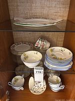 Cabinet view showing platter, stacks of plates, teacups, footed bowl