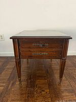 Front view of wooden side table showing glass top, drawer front, legs