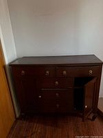 Front view of dark wood sideboard showing drawers, cabinet door, hardware, and feet
