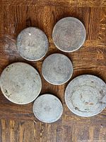 Six round metal trivets on wooden floor, showing size variation and wear