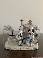 Front and side view of porcelain carriage group showing figures, horse, blue and gold decoration