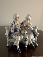 Full view of porcelain figurine showing Victorian couple seated on settee with blue floral decoration and gold accents