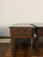 Front view of wooden side table showing carved drawer and turned legs