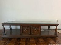 Front view showing glass top, wooden frame, central cabinet doors with ring pulls, and open side shelves