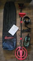 Full kit laid out: metal detector assembled, carry bag, manual, headphones, cable, digging tool