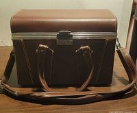 Closed brown hard camera case with shoulder strap