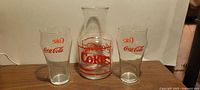 Front view of Coca-Cola glass carafe flanked by two Coke tumblers