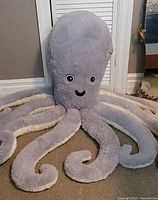 Front view of oversized light grey octopus plush showing head, eyes, mouth, and eight curled tentacles
