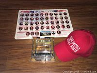Photo showing the lot spread out on a wooden floor including the Presidents chart poster, the red MAGA hat, and the Trump Executive Debit Card replica.