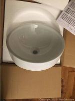 White round ceramic vessel sink inside opened cardboard box with foam packaging and instruction paper.