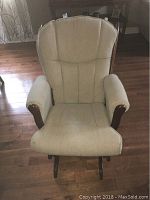 Front view of the cream upholstered rocker glider chair showcasing padded cushioning and wooden armrests.