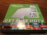 Photo of the Mohu Leaf fifty indoor amplified HDTV antenna box in green and white with logos of TV networks, and a 3-way splitter placed on top.