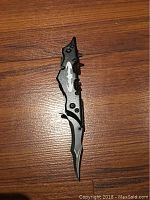Black and silver Batman batarang knife with sharp blade and bat logo design placed on wooden floor.