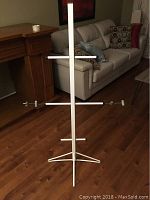 Image of aluminum hockey equipment drying rack standing on hardwood floor near furniture, showing the overall structure with arms for hanging hockey gear.