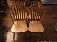 Four solid wood dining chairs arranged together on a hardwood floor, showing overall shape and finish.