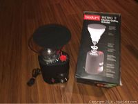 Electric coffee grinder placed beside its original box on wooden floor, showing the front and top view including the clear hopper and control dial.