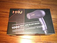 Closed box of MHU Mini Pro Hair Dryer, showing product image and branding including 1000 watt power, metallic black color, rubber comfort finish, concentrator nozzle and one year warranty.