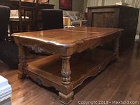 Front side view of a solid wood coffee table with carved legs and decorative apron, showing the lower shelf.