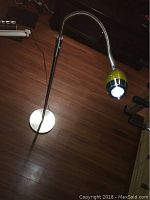 Floor standing reading lamp on wooden floor showing flexible neck and oval lamp head with yellow and silver finish.