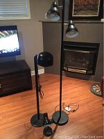 Three black lamps: two floor lamps with dual adjustable bell-shaped heads and one desk lamp with a dome-shaped adjustable head in a living room setting.