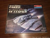 Photo of box front showing Space Fighter Raider spacecraft artwork from Battlestar Galactica, with English and French text and Monogram branding.
