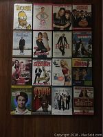 Photo showing all 16 comedy DVD titles arranged in four rows of four across a wooden floor.