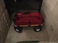 Front-side angle view of red fabric lined wagon with wooden sides and rubber wheels showing full structure and handle.